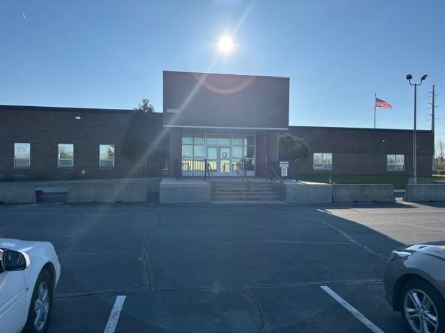 Two cars parked in front of a large building with flag and bright sun.