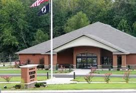 Building with gray roof and brown walls, two flags, and green lawn.