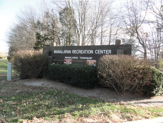 Sign for Manalapan Recreation Center surrounded by bushes and bare trees.