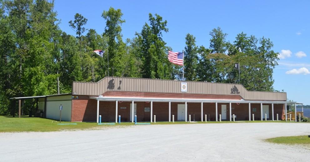 Large building with brown roof, two flags, and trees in background.