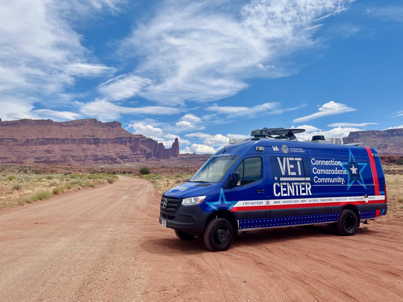 Blue "VET Center" van on dirt road with desert hills in background.