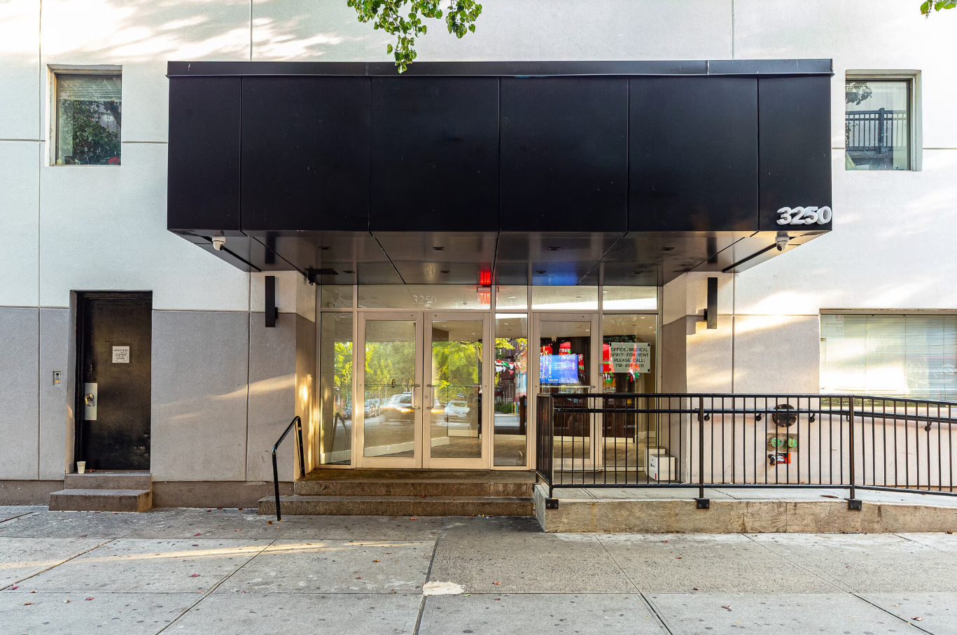 Modern building entrance with black canopy, glass doors, and railings.