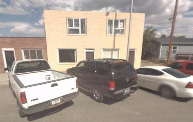 White pickup truck, black SUV, and white sedan parked in front of a yellow building.