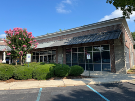 Modern storefront with glass windows, black awning, and greenery in front.