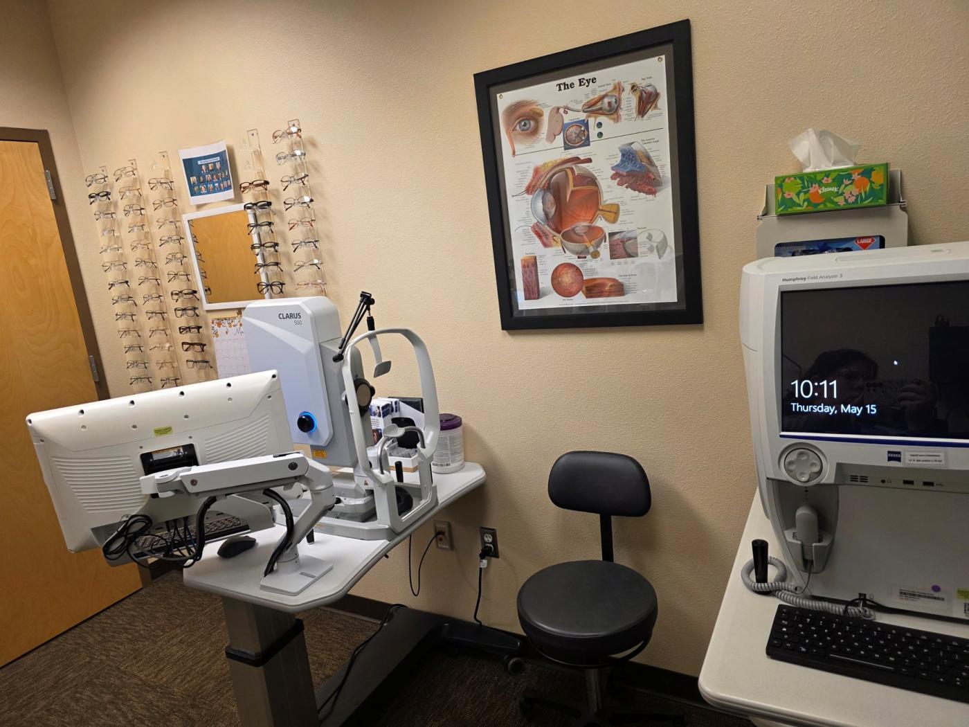 Exam room with medical equipment, chair, and eye diagram on wall.